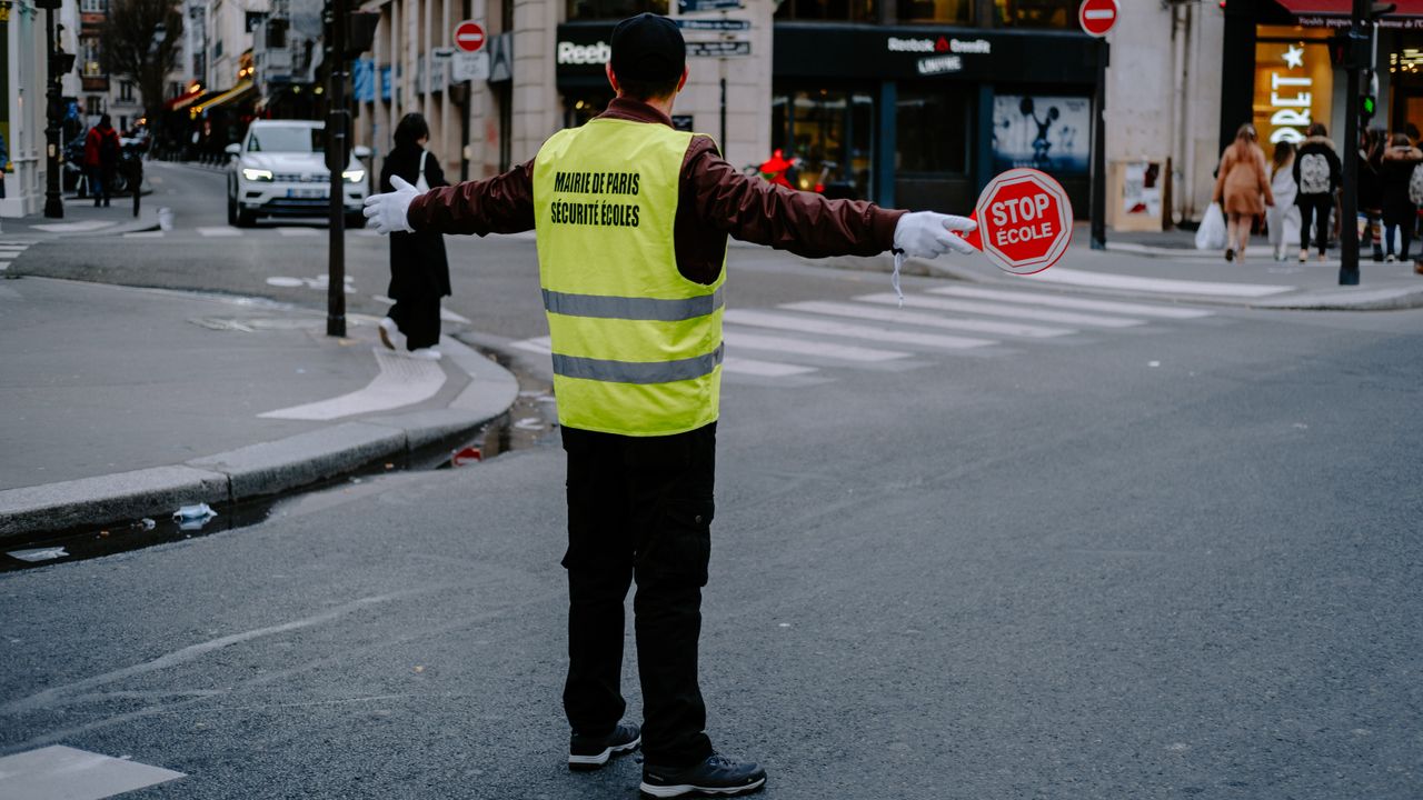 Back view of a crossing guard holding a stop sign in a busy city street.