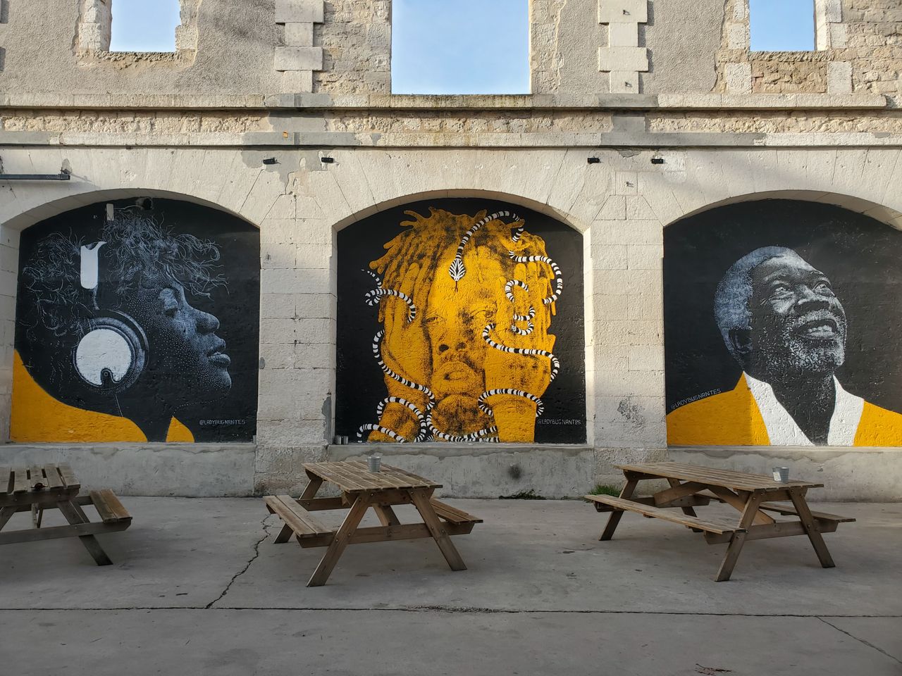 Colorful murals adorn an outdoor stone wall with wooden benches nearby.