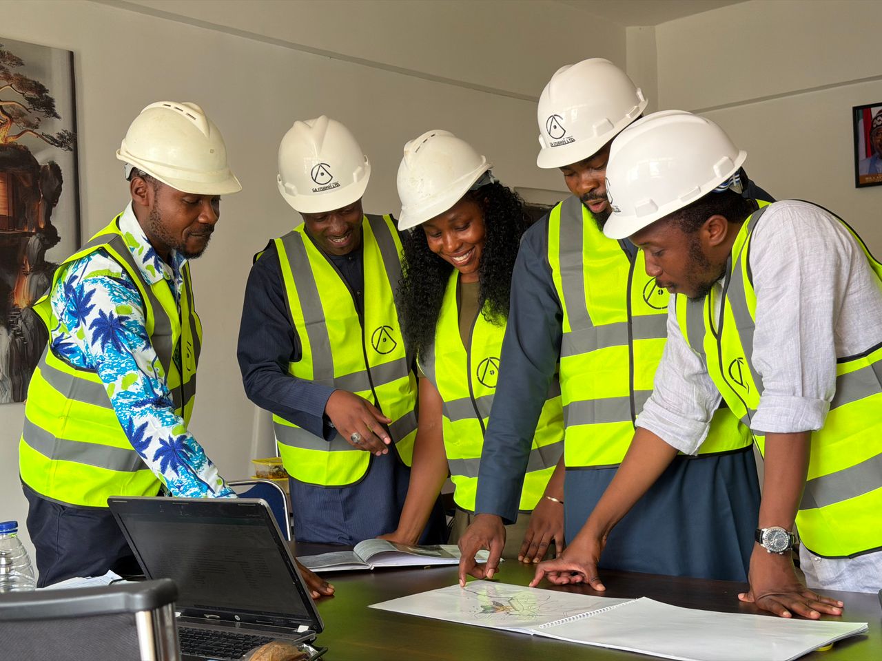 Group of engineers in safety gear discussing architectural blueprints in an office.