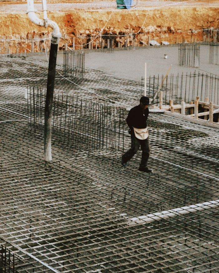 A worker walks on a construction site with reinforced concrete and steel bars, depicting industrial development.
