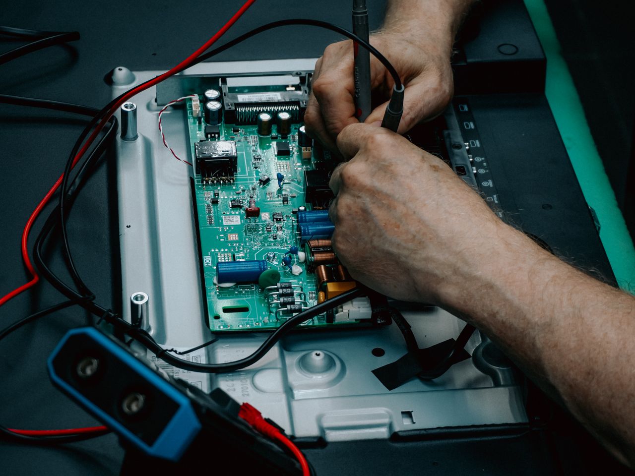 Close-up of hands repairing electronic circuit board, showcasing detailed technology work.
