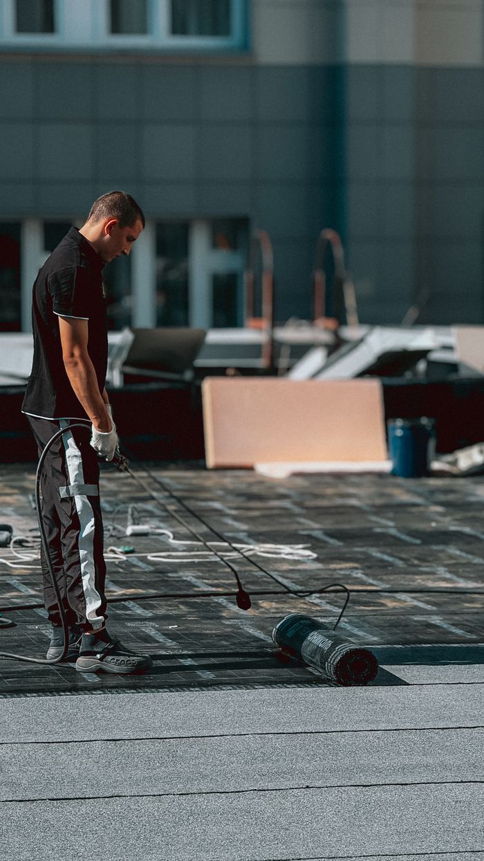 A construction worker applying a waterproofing coat on a rooftop with a roller during daytime.