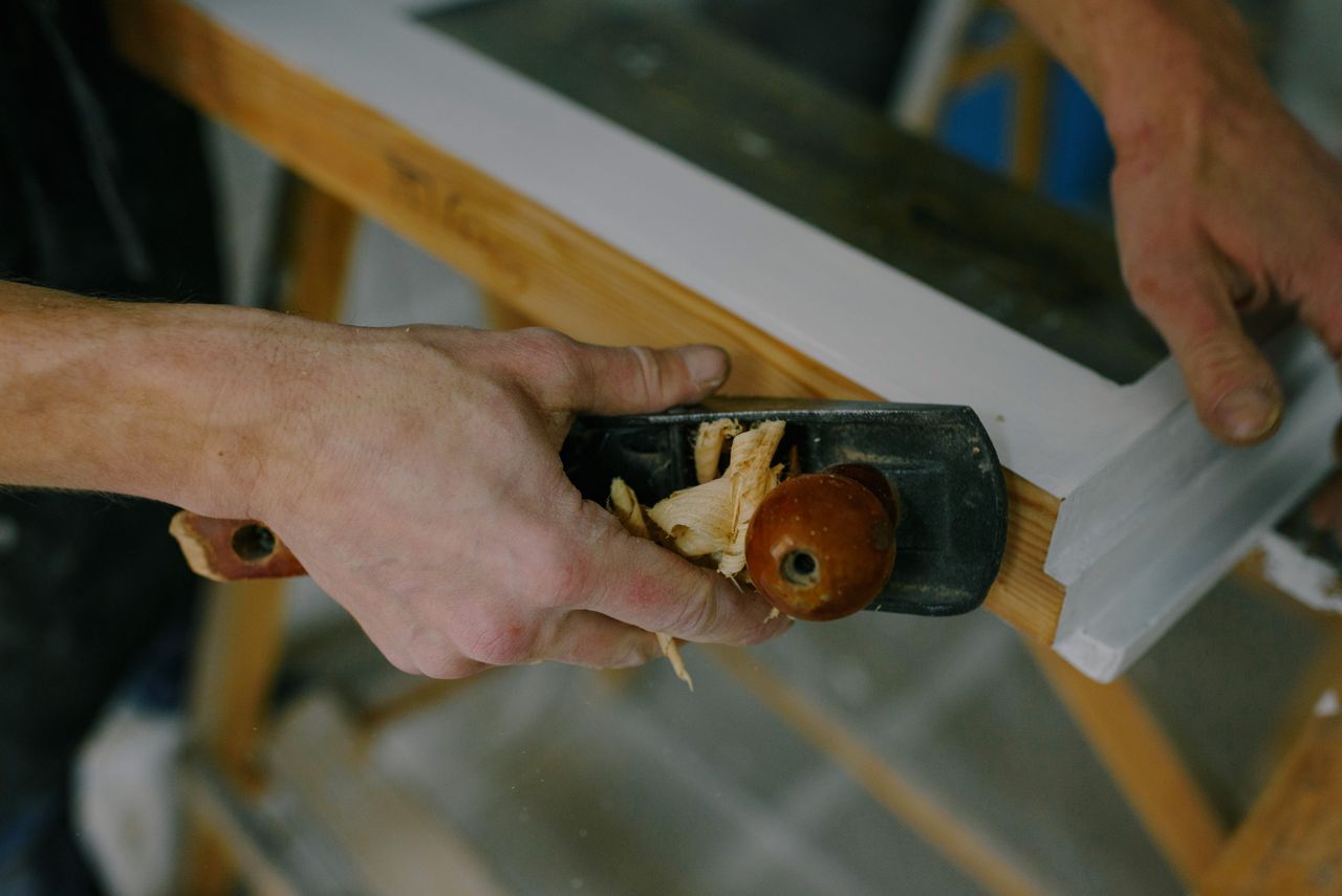 From above of crop anonymous joiner cutting wooden frame with manual jack plane at work