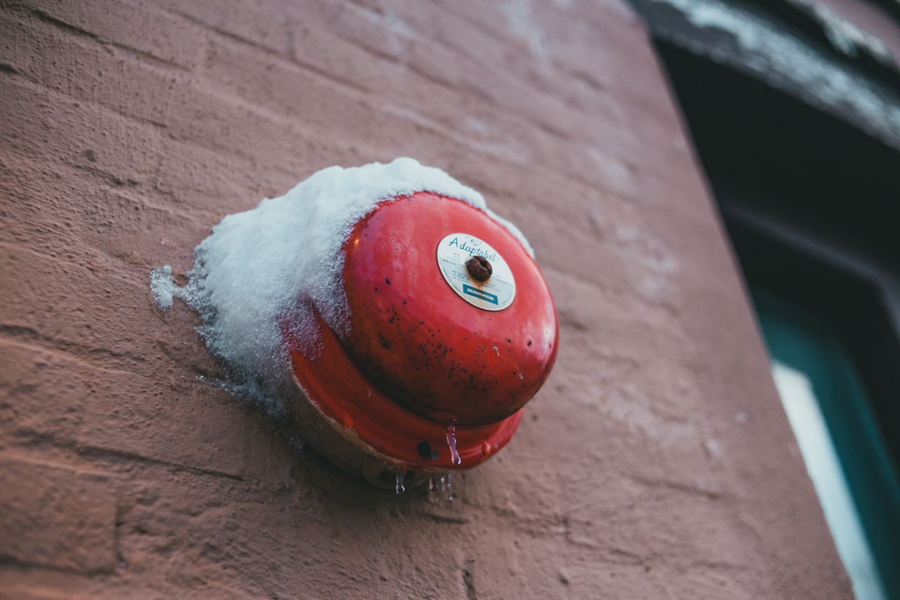 From below of fire alarm button with snow and icicles on rough wall of house in winter town